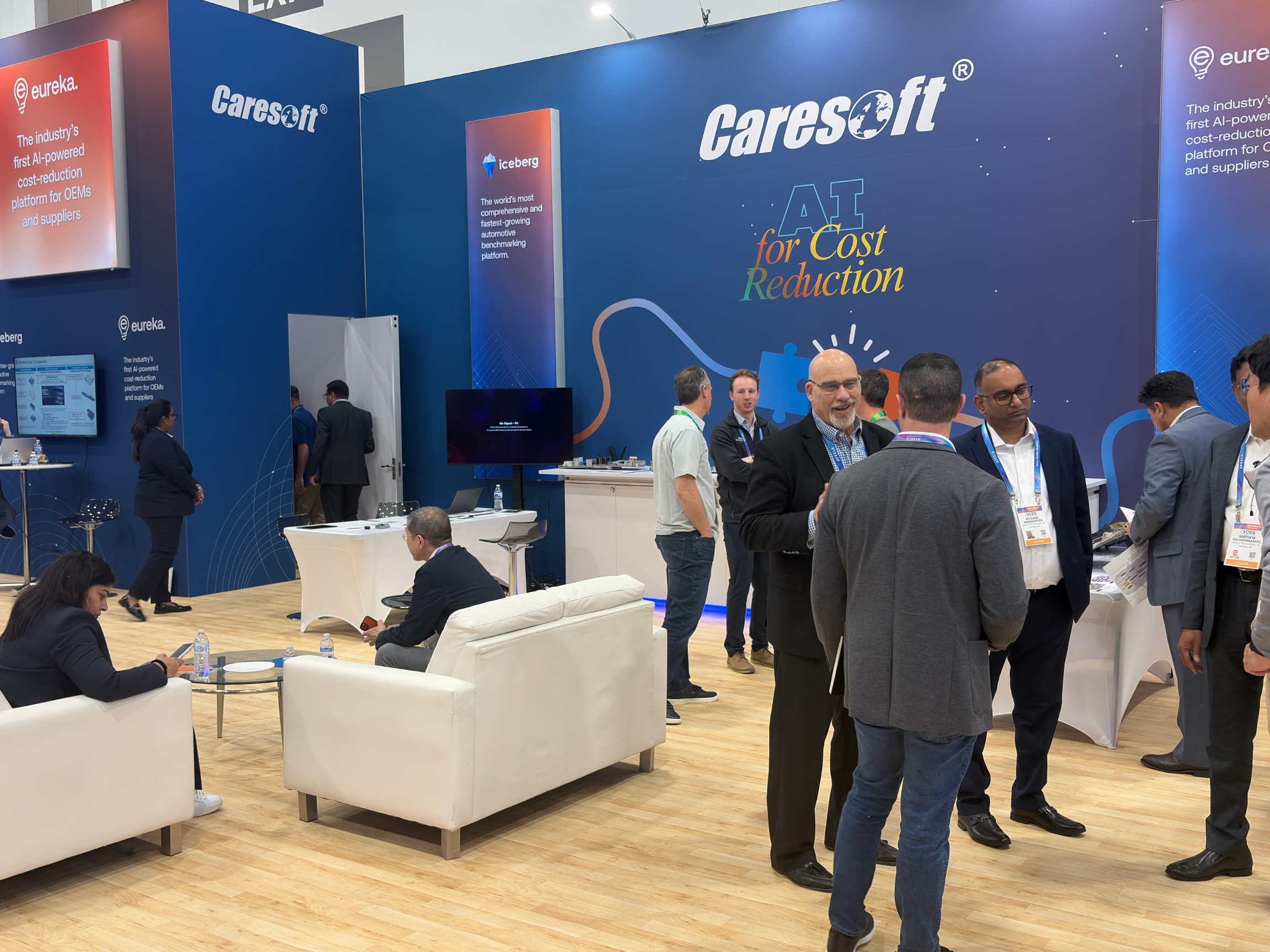 A CareSoft exhibition booth at an industry event, with several people networking in front of displays promoting AI-powered cost reduction, automotive benchmarking, and supplier solutions.