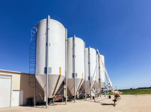A modern farm with a building used for raising pigs accompanied with a metal grain bin used for feeding the livestock.
