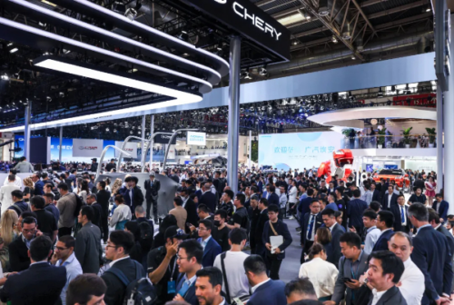 Large crowd at an auto show with Chery booths and glossy car displays under bright overhead lights.