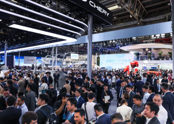 Large crowd at an auto show with Chery booths and glossy car displays under bright overhead lights.