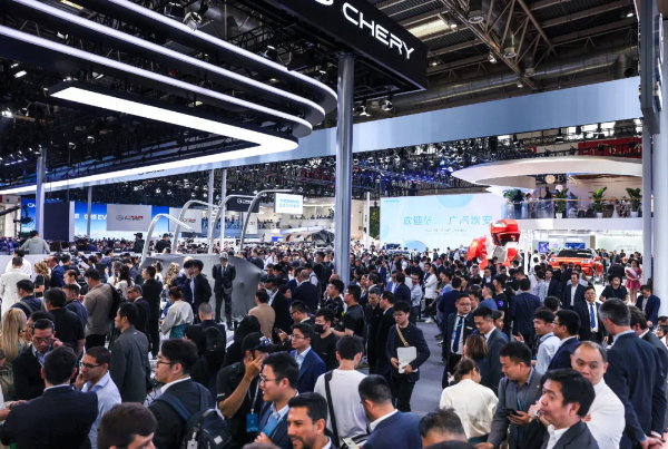 Large crowd at an auto show with Chery booths and glossy car displays under bright overhead lights.
