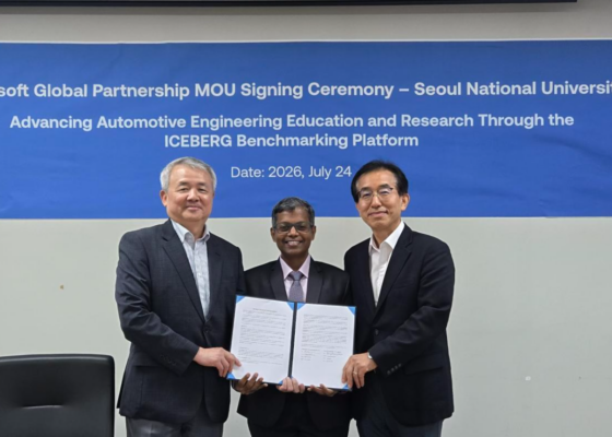 Three men in suits stand together, holding a signed document in front of a blue banner used for a signing ceremony.