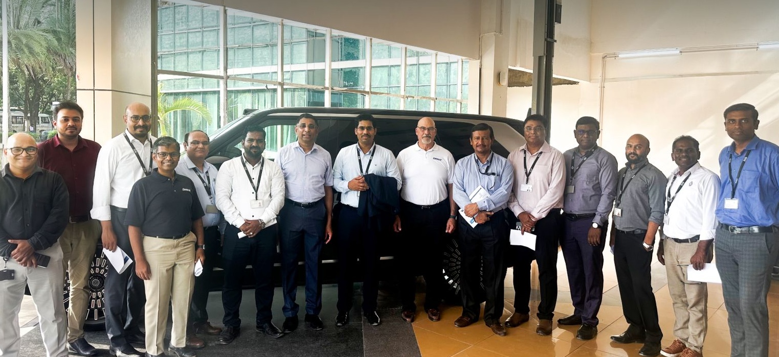 Group of 15 professionals posing in a showroom next to a dark SUV, dressed in business casual attire and name badges.
